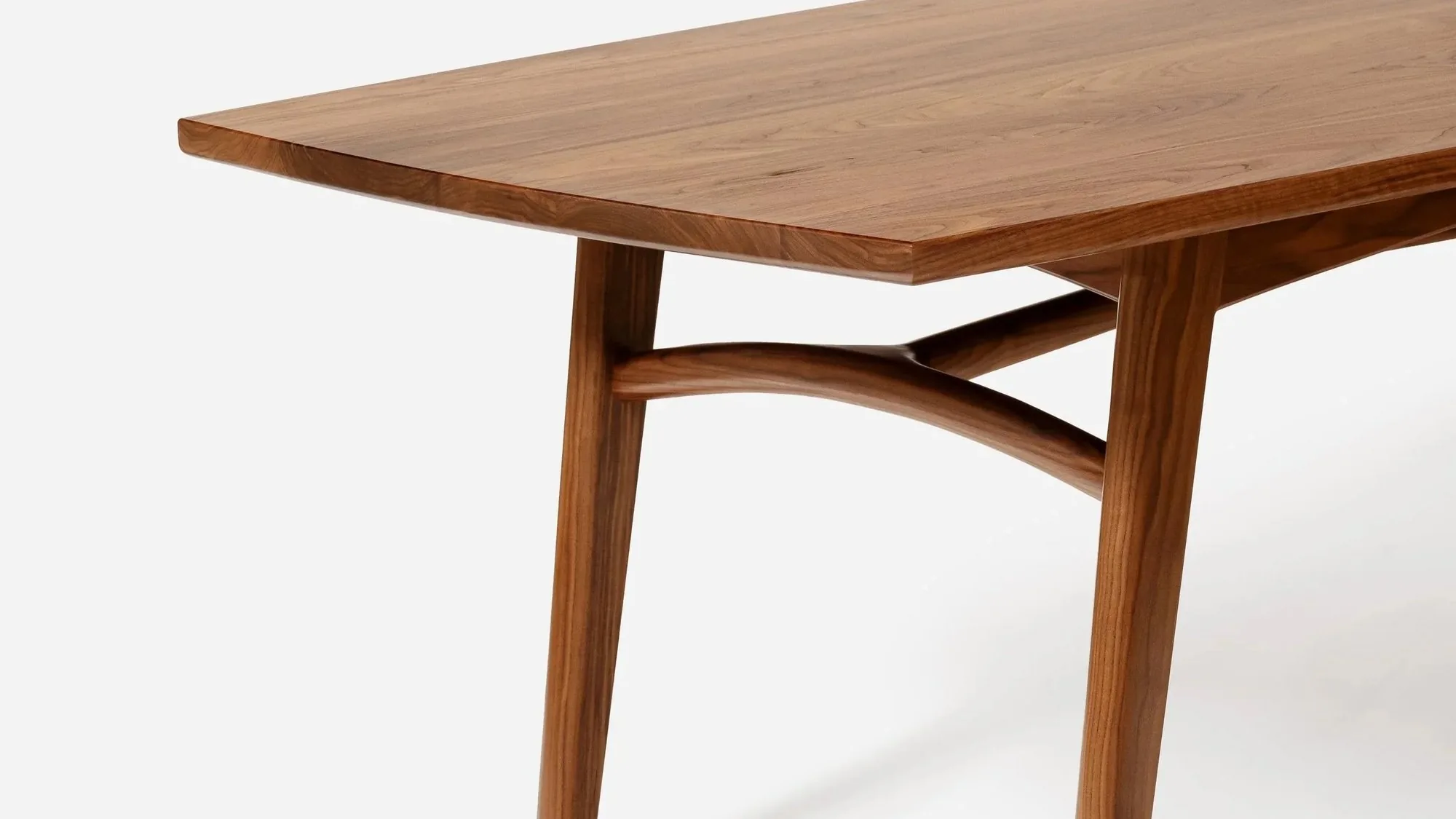 Close view of a walnut dining table edge and shaped leg.