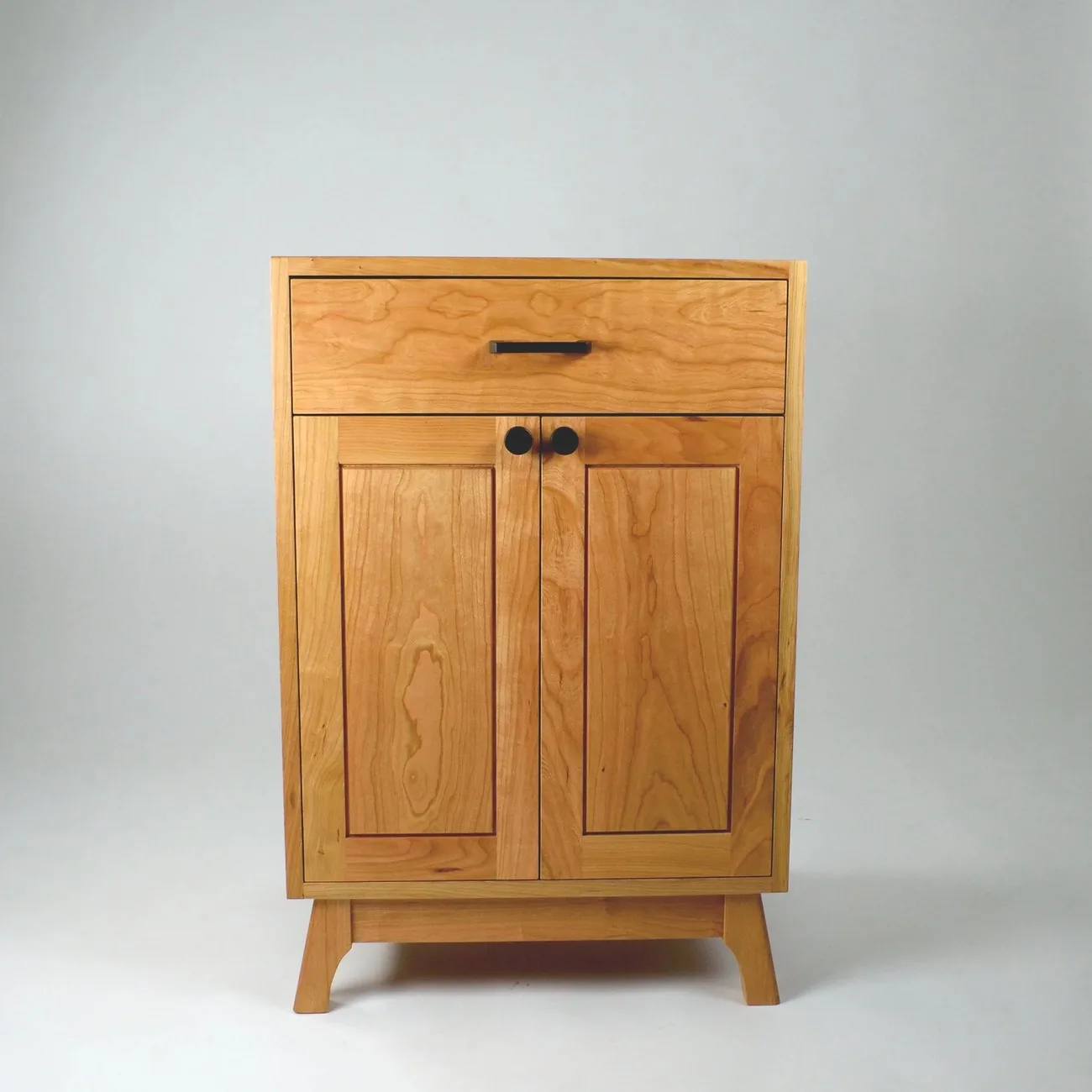 A cherry cabinet with two panelled doors and a single drawer.