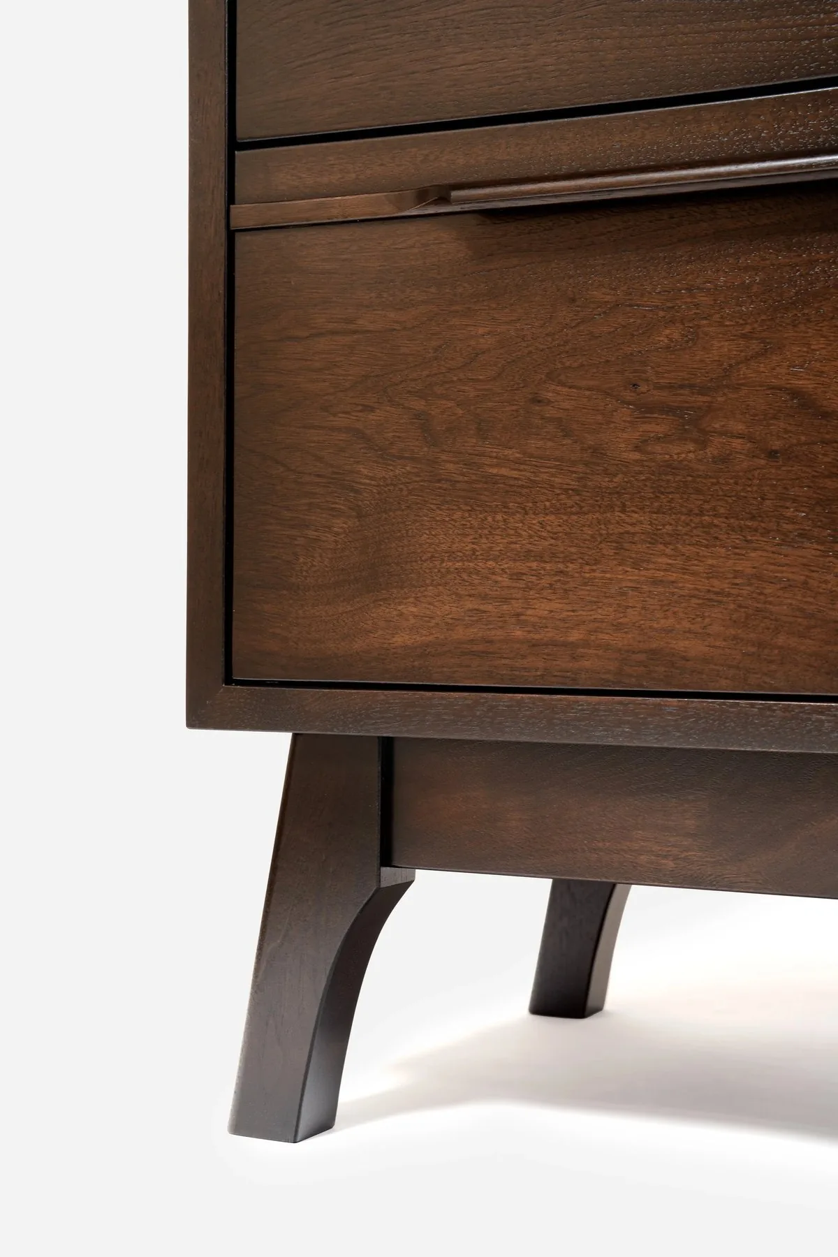 A walnut case piece with a shaped foot and a drawer front showing open grain.